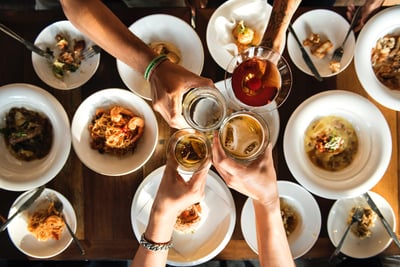 4 people cheering over plates of yummy food