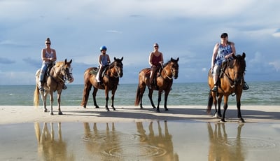 4 people horseback riding on the beach