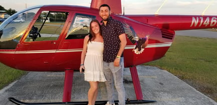 Couple smiling in front of red helicopter