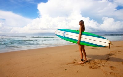 girl holding a bue, green and white surfboard on the beach