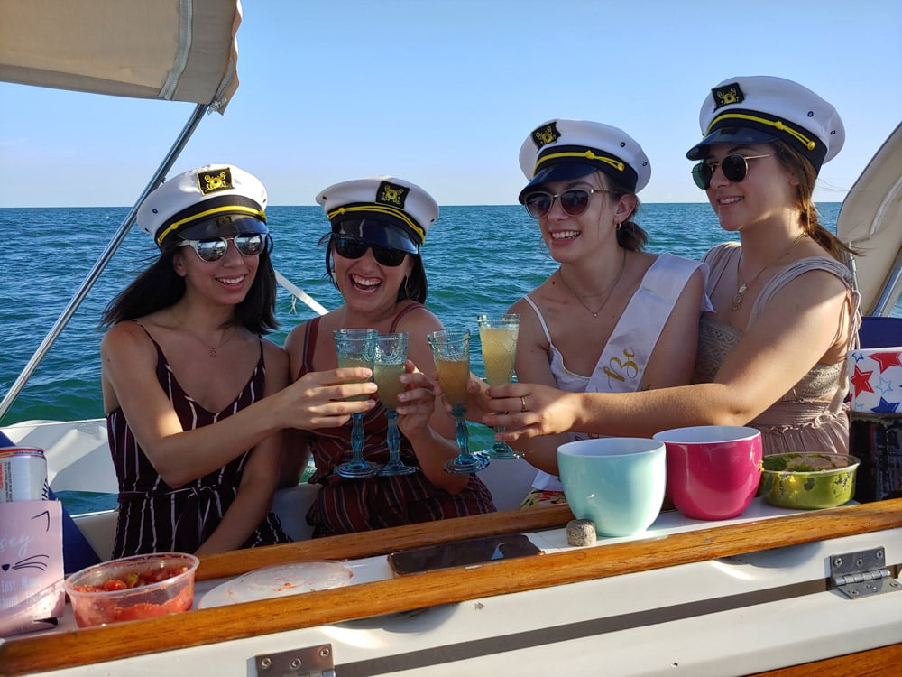 Four ladies wearing captain hats drinking on a sail boat