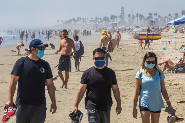 Three people wearing face masks on a sandy beach in Florida