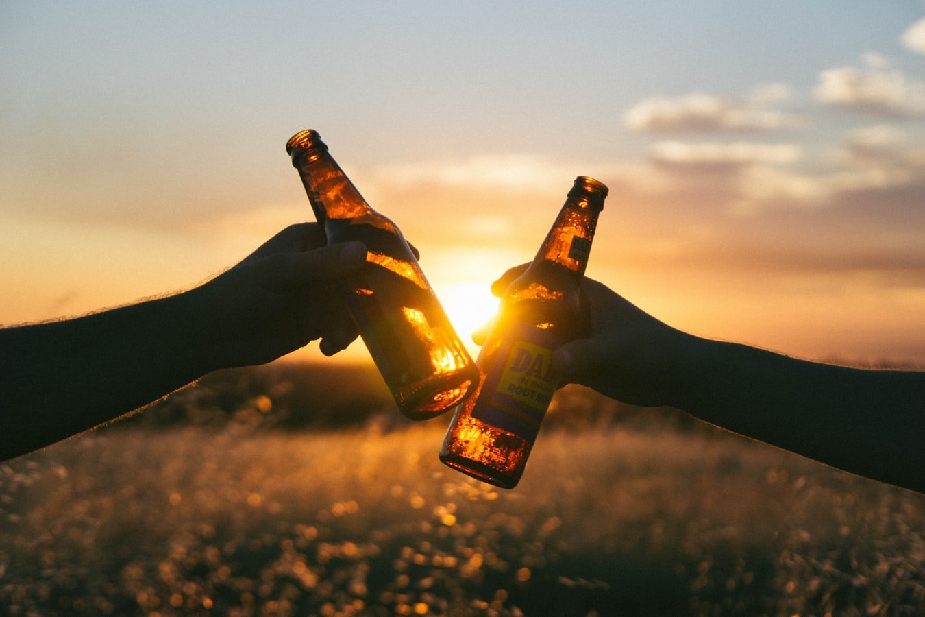 two beers clinking with a sunset behind them